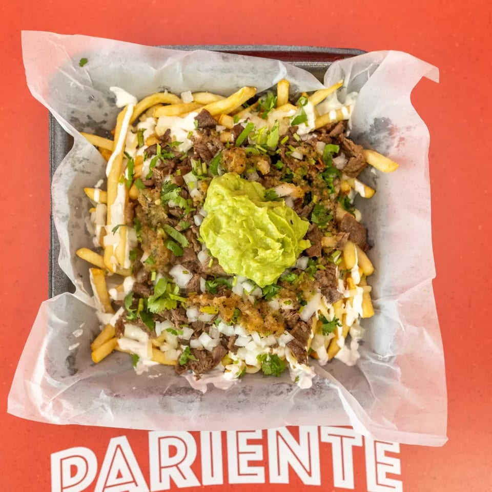 Carne asada fries topped with guacamole, sour cream, cilantro, and onions in a black tray.