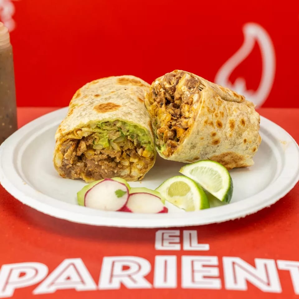 Two burritos, one cut open to show meat and guacamole, with lime and radish slices on a white plate.